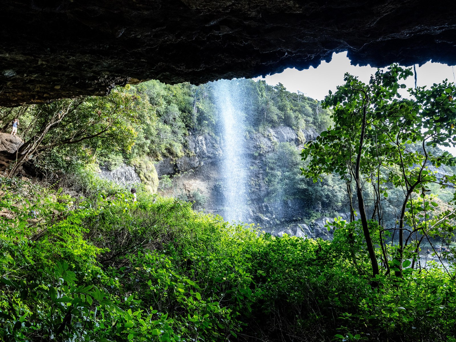 A waterfall seen from beneath the rock overhang behind it.